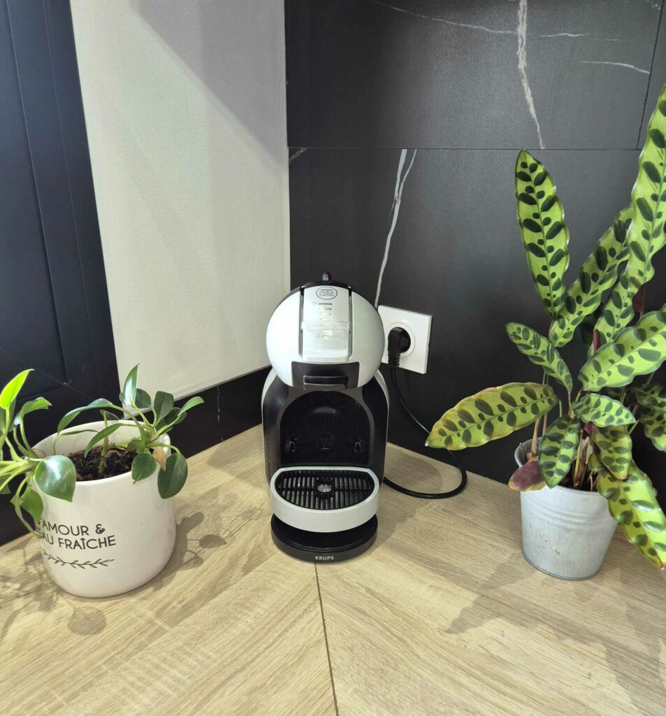 Machine à café Dolce Gusto sur plan de travail en bois, entourée de plantes vertes décoratives dans une cuisine moderne