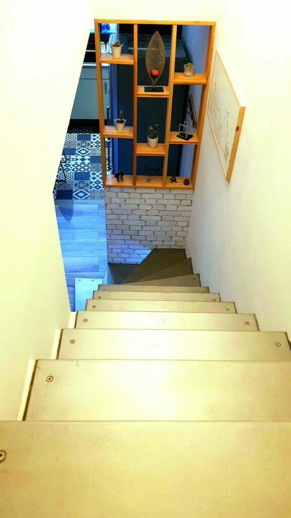 Vue plongeante depuis l'escalier métallique montrant une étagère de séparation design en bois