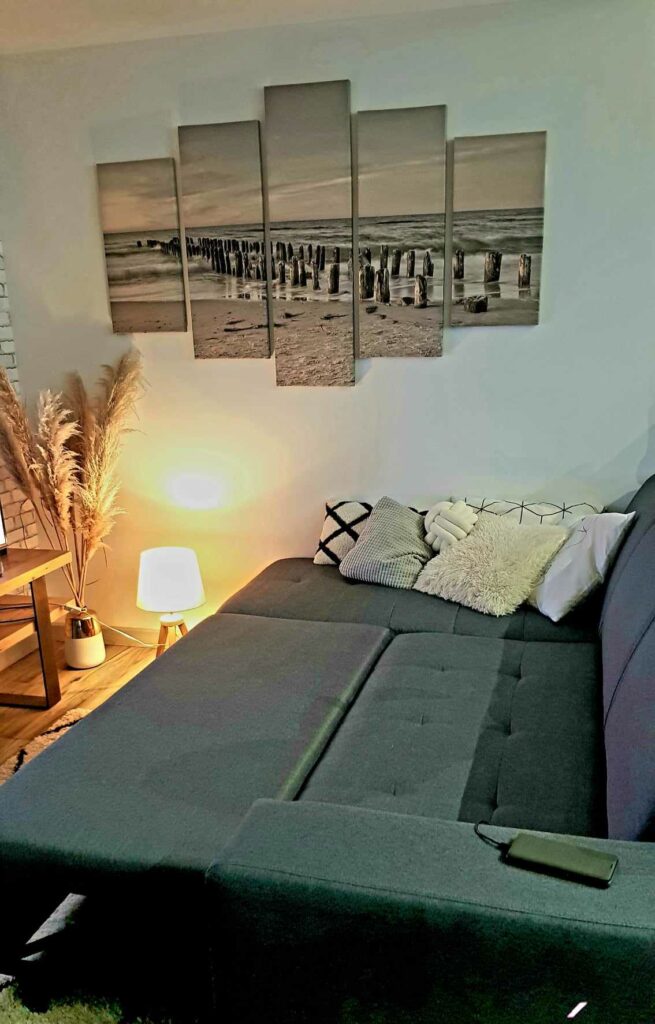 Vue détaillée du canapé gris avec des coussins décoratifs, lampe d'appoint chaleureuse et herbes de pampa en décoration