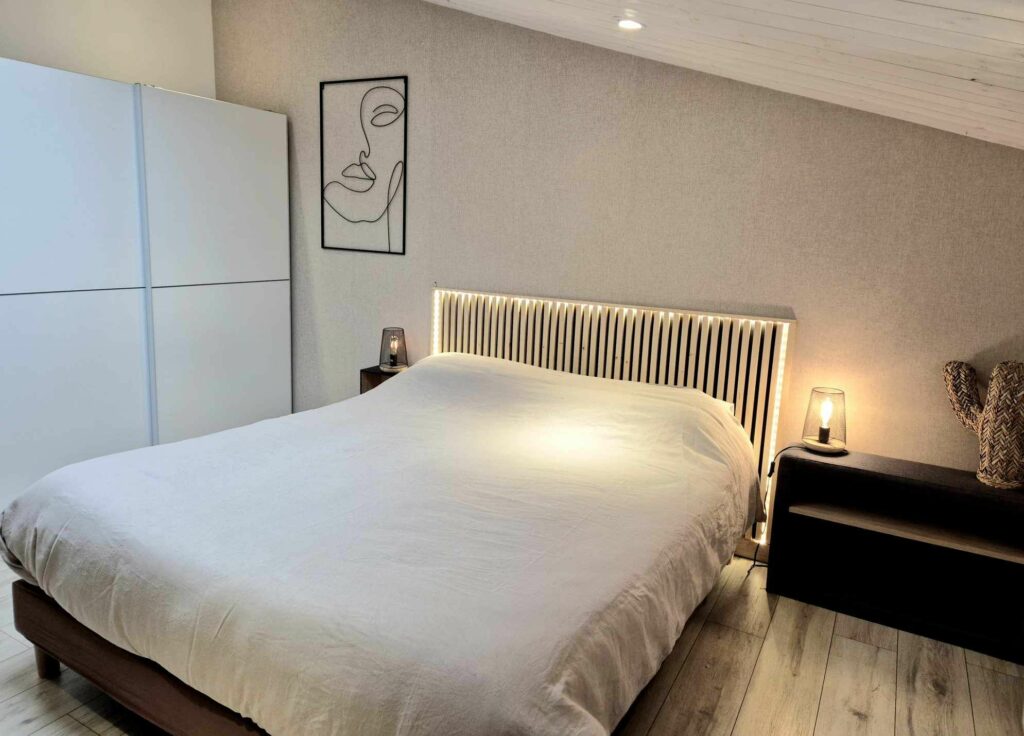 Lit double avec une tête de lit originale en tasseaux de bois rétroéclairés et lampe de chevet design