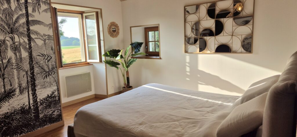 Vue d'ensemble d'une chambre avec parquet châtaigner, murs blancs, décoration tropicale et fenêtres en bois