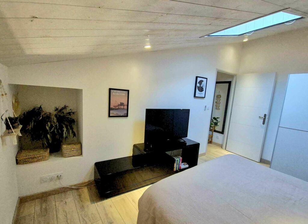Chambre à l'étage avec fenêtre de toit (velux), télévision, rangements et décoration épurée