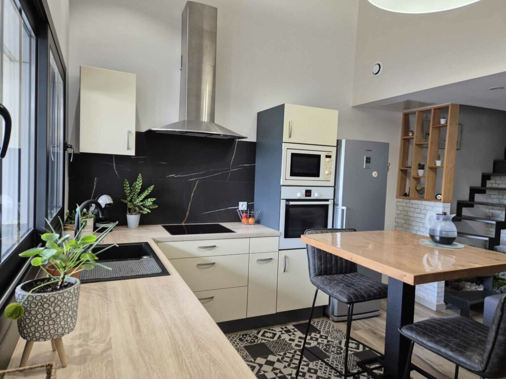 Cuisine ouverte moderne avec plan de travail en bois clair, crédence noire marbrée, plaque de cuisson, fours encastrés et table haute pour les repas