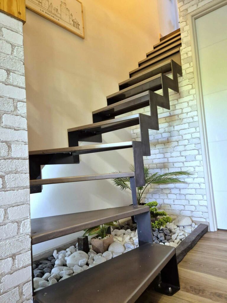 Escalier moderne en métal avec en dessous un espace zen éclairé composé de galets blancs et de plantes vertes