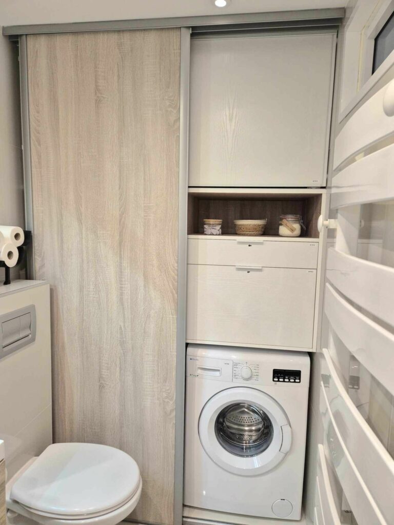 Salle d'eau optimisée avec lave-linge intégré dans un placard, rangements blancs et modernes, WC suspendu