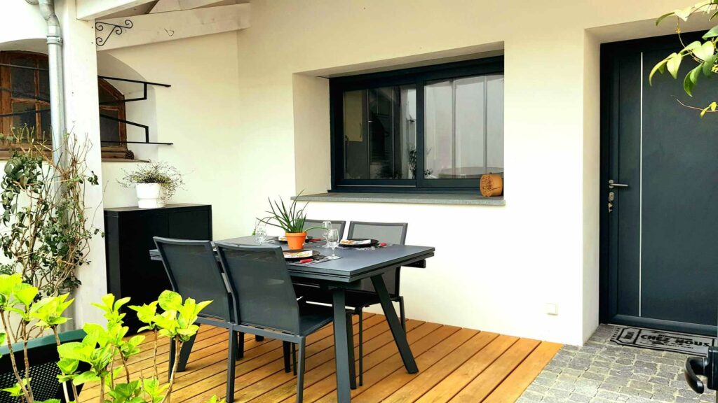 Préau extérieur avec terrasse en bois, table et chaises modernes, entouré de murs blancs