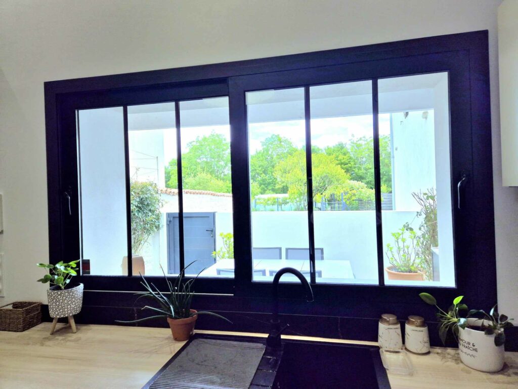 Grande fenêtre de cuisine anthracite offrant une vue sur une terrasse privée aménagée et de la verdure