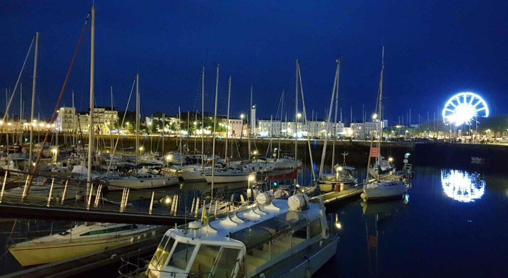 Port de plaisance de La Rochelle de nuit avec de nombreux mats de voiliers et la Grande Roue illuminée au loin