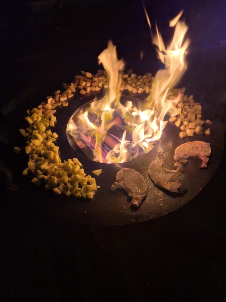 Cuisson de viandes et de légumes sur un Ofyr entouré de flammes vives à la nuit tombée