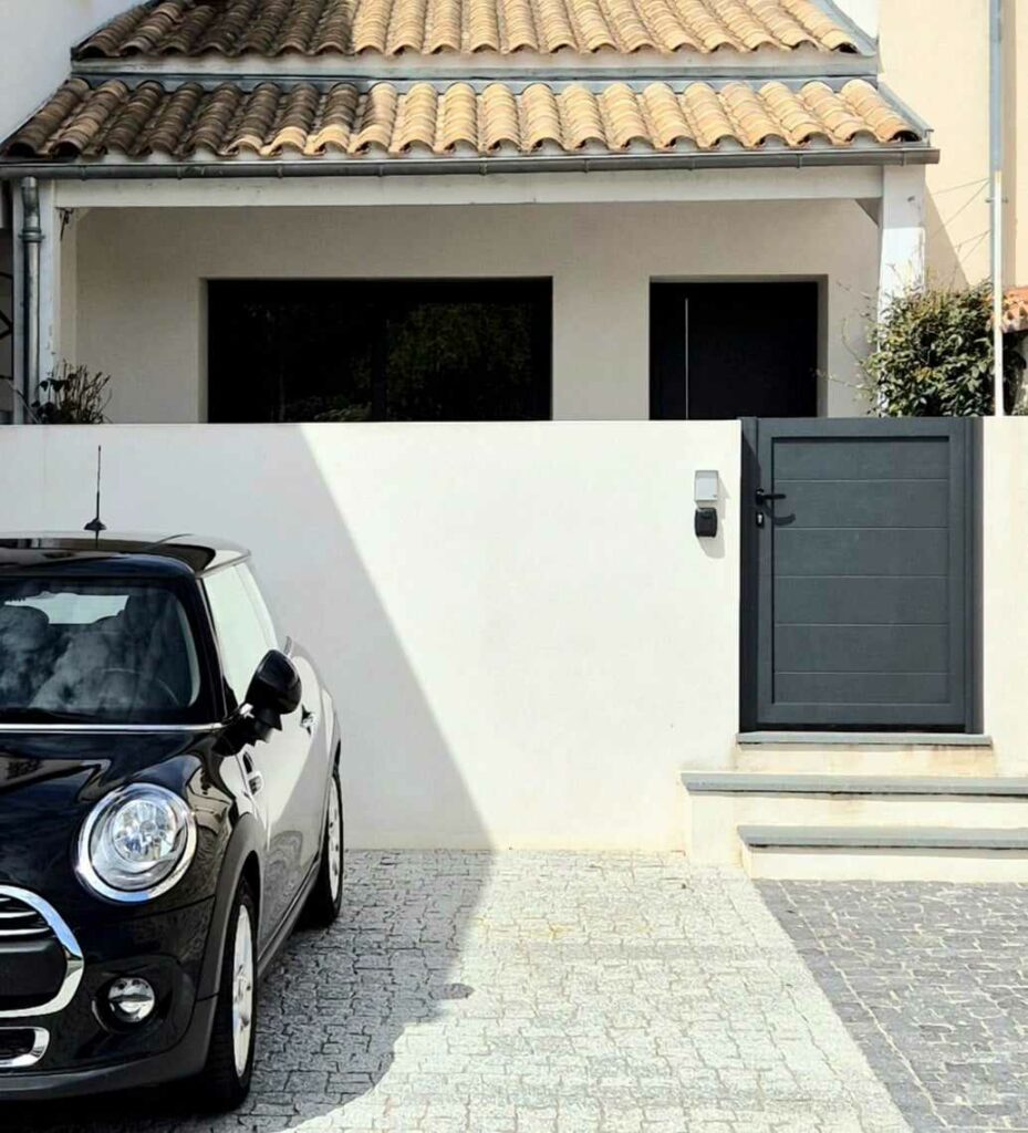 Façade d'une maison de vacances moderne avec un muret blanc, un portillon gris anthracite et deux places de parking privées devant l'entrée