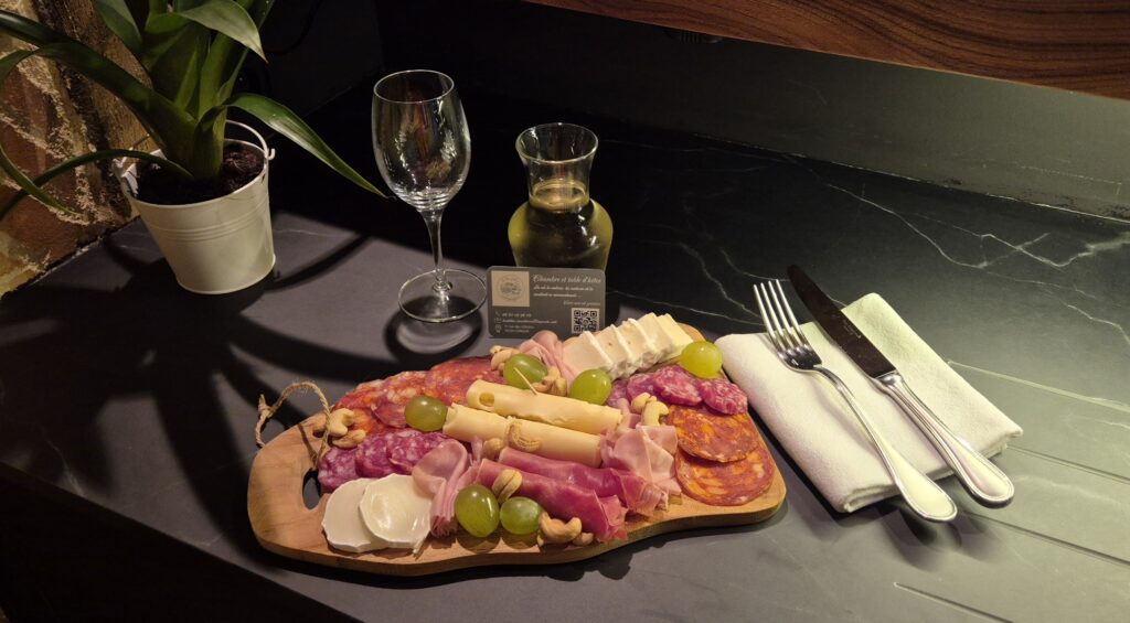 Planche de charcuterie et assortiment de fromages accompagné d'un verre de vin blanc sur un plan de travail sombre