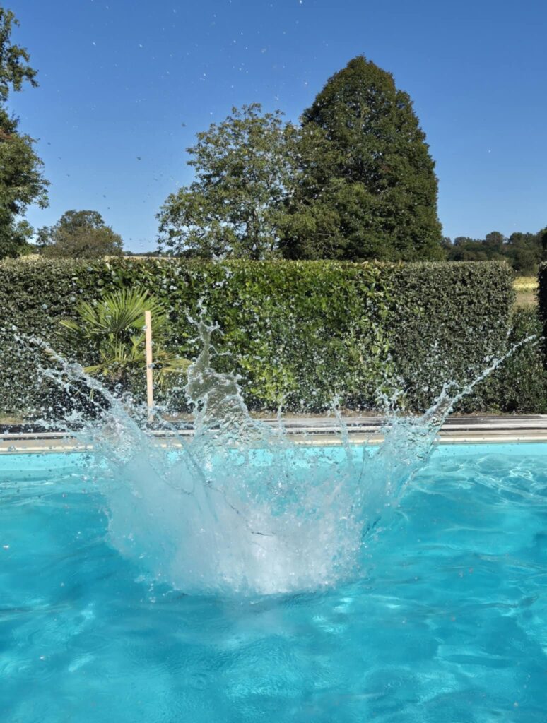 Grand jet d'eau provoqué par un plongeon dans une piscine turquoise sous un ciel radieux