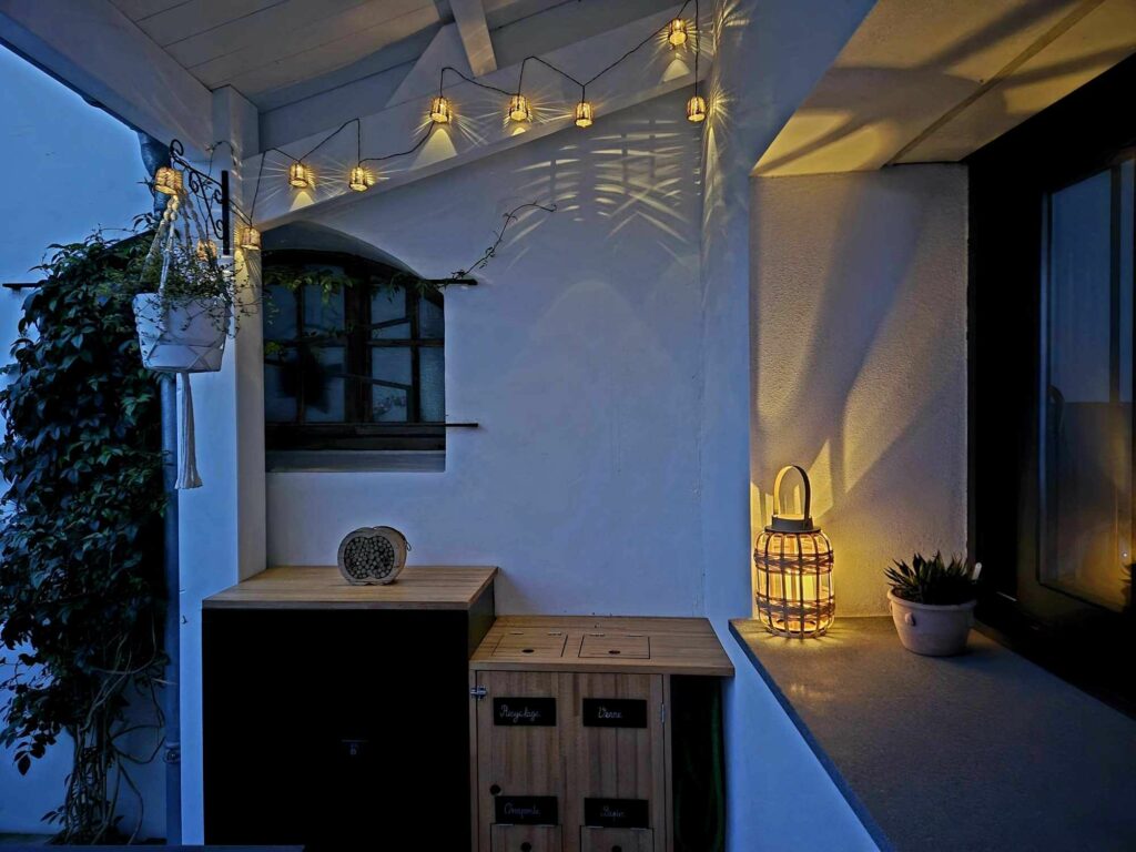 Terrasse de nuit éclairée par une guirlande lumineuse et une lanterne en rotin, créant une atmosphère cosy et cocooning