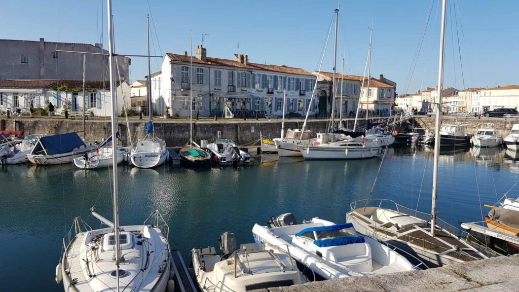 Vue sur le port paisible de Saint-Martin de Ré avec des petits bateaux amarrés le long du quai. En arrière plan, des bâtiments anciens typiques de l'île