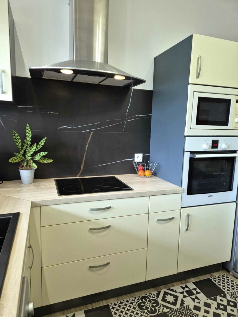 Vue sur l'aménagement d'un cuisine moderne. Plan de travail en bois clair, crédence noire marbrée, plaque de cuisson, fours encastrés et hotte