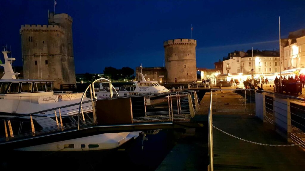Le vieux port de la Rochelle de nuit avec la Tour de la Chaîne et la tour Saint-Nicolas illuminées avec des bateaux en premier plan